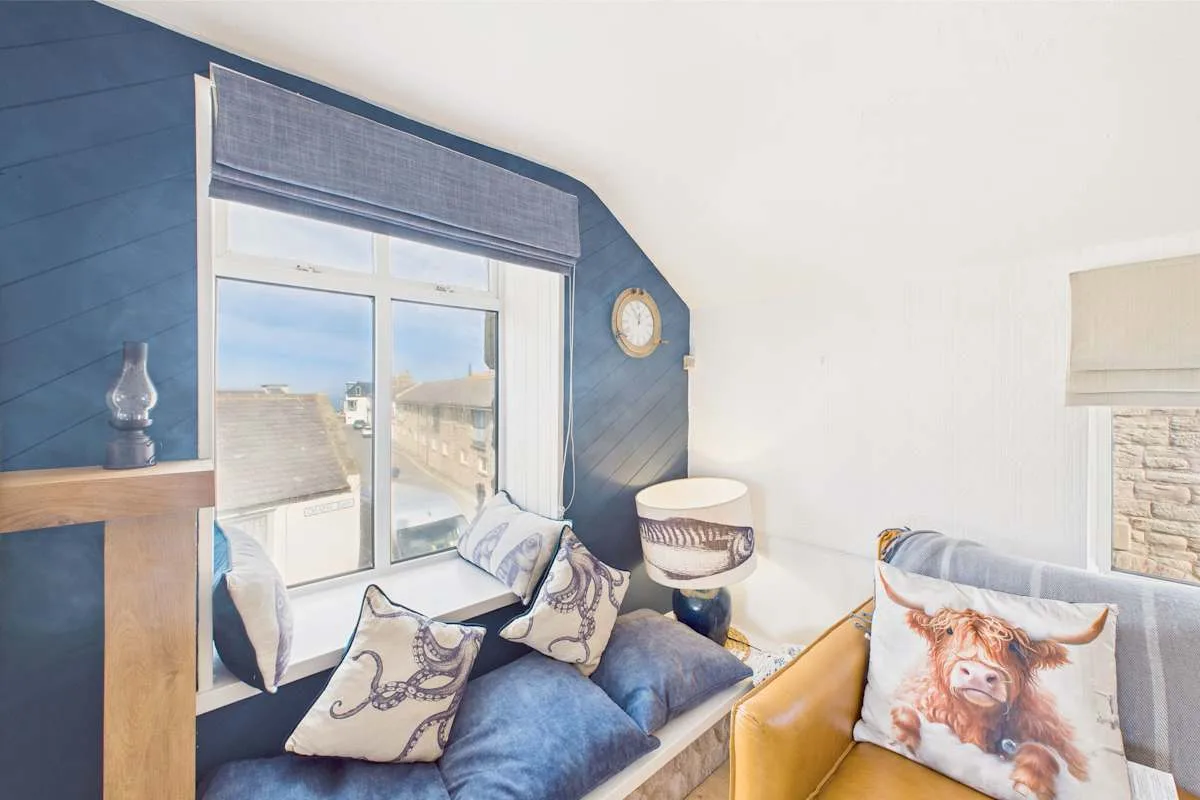 Una zona de estar junto a una ventana grande tiene cojines azules y una silla amarilla.