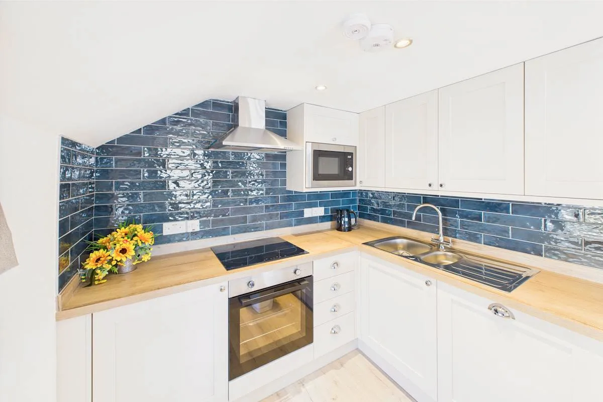 Una cocina luminosa con armarios blancos, encimeras de madera y azulejos azul oscuro.