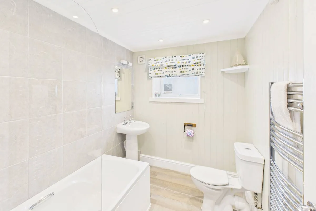 Un baño luminoso con bañera, lavabo con pedestal, inodoro y toallero.