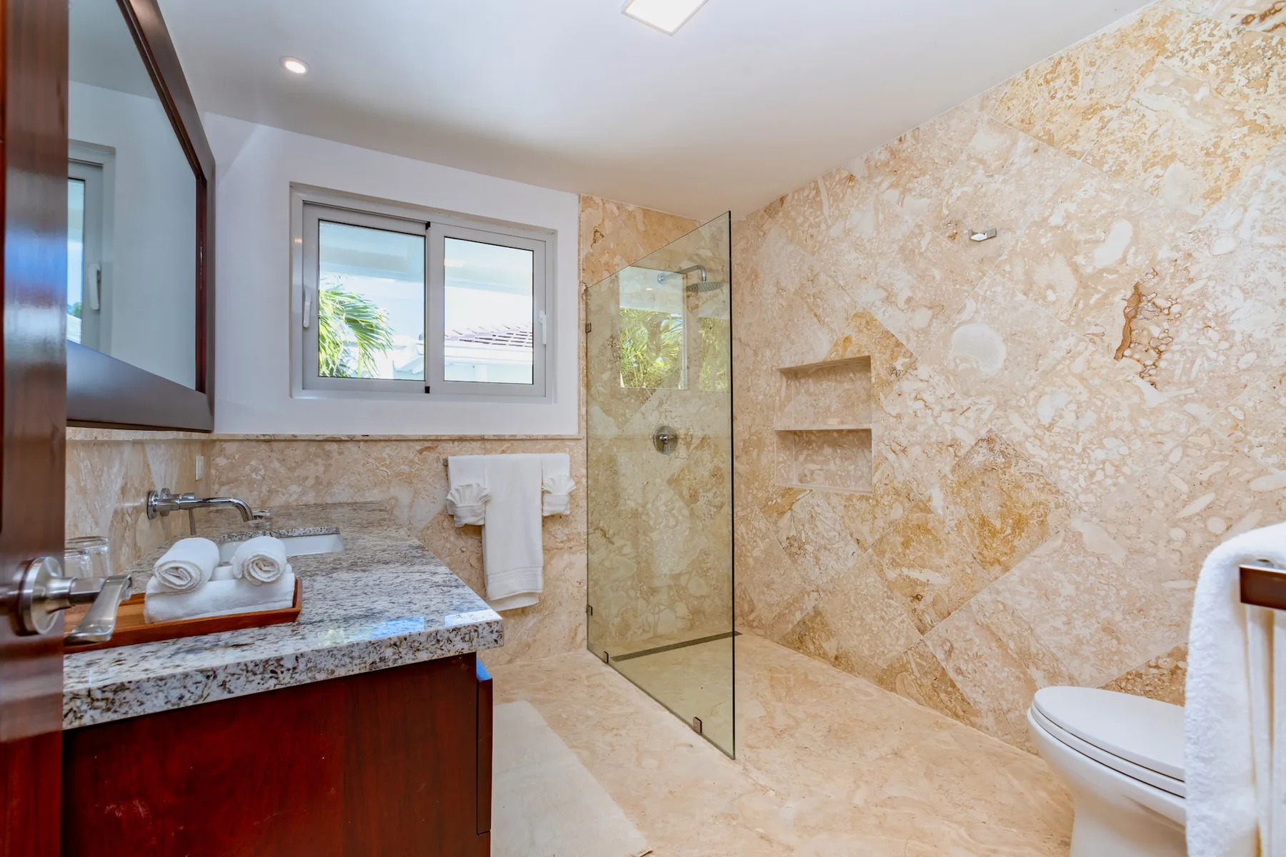 A bathroom with a glass shower, vanity, and window.