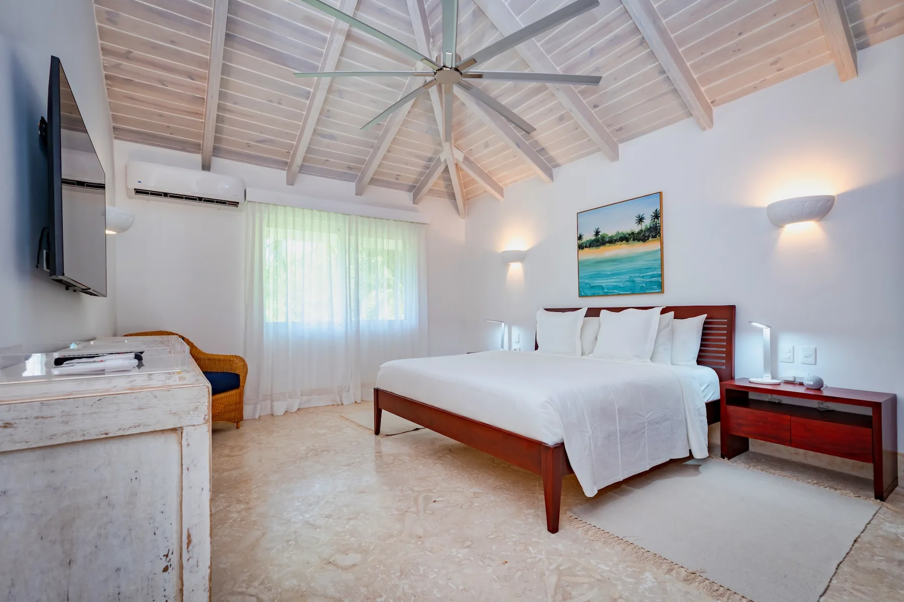 A bright bedroom with a large bed and a window with sheer curtains.