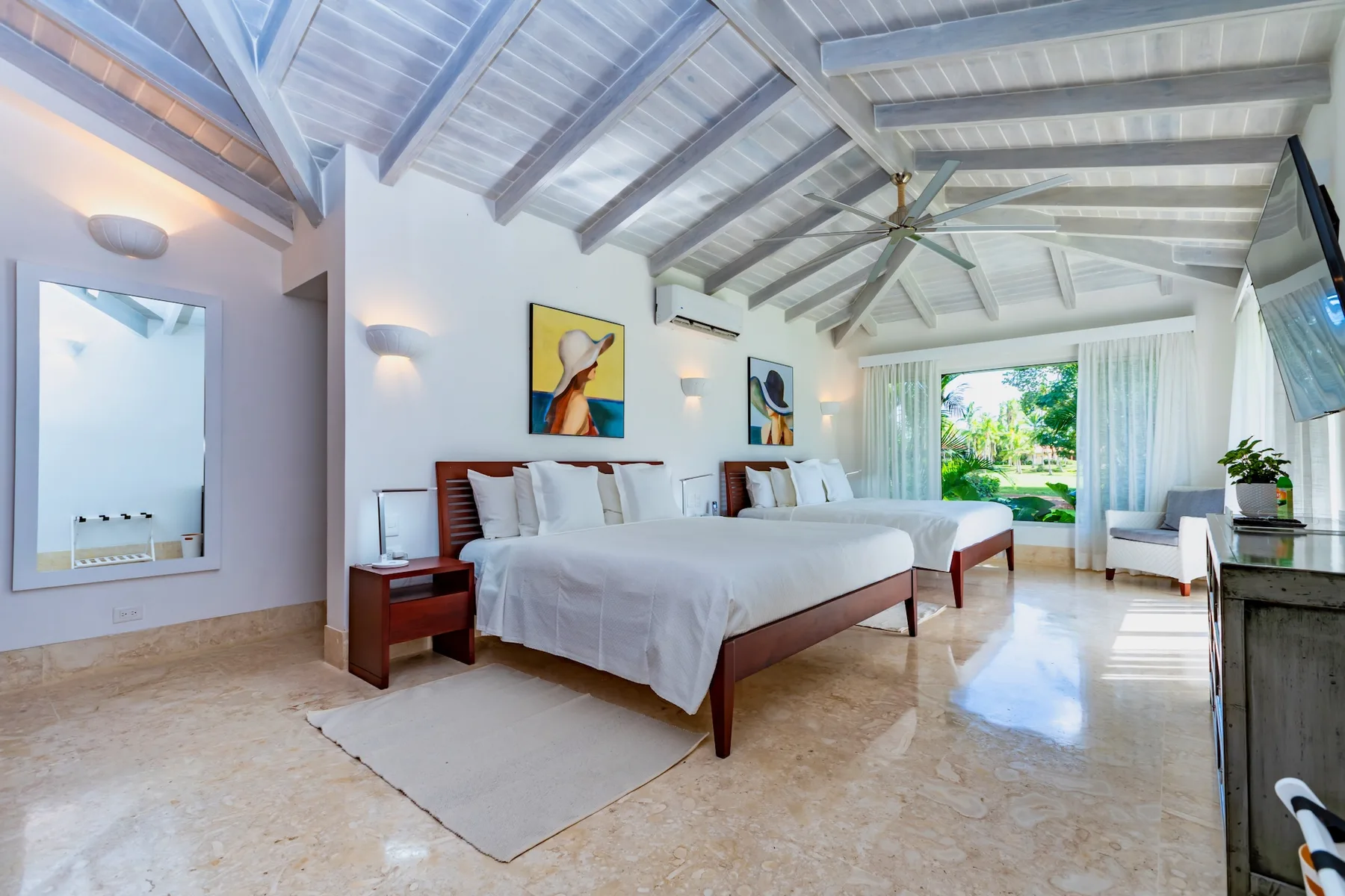 A bright bedroom with two beds and a high, beamed ceiling.