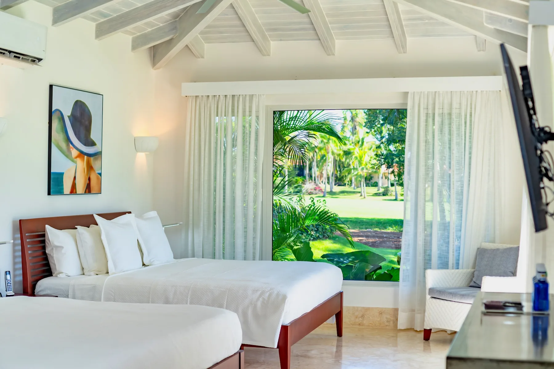 A bright bedroom with white bedding and a large window overlooking greenery.