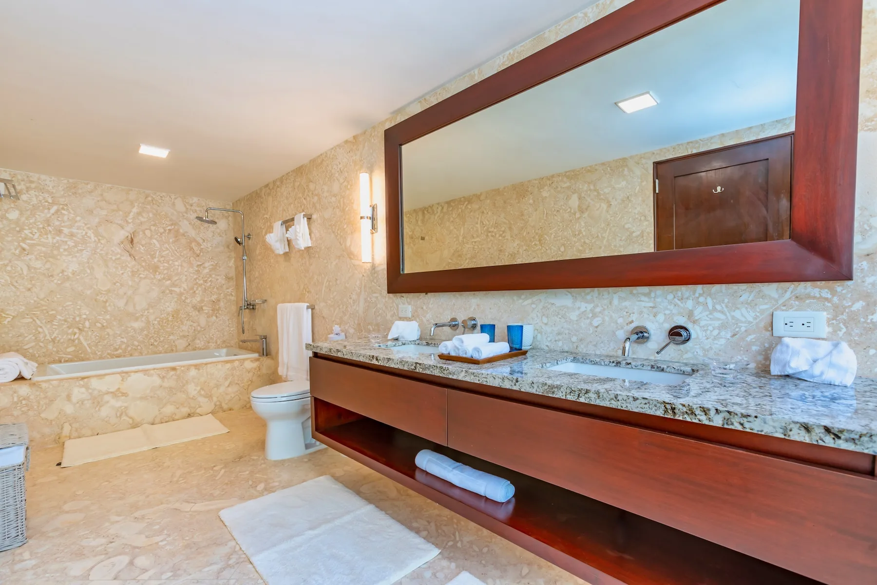 A bathroom with a bathtub, toilet, and long vanity beneath a large mirror.