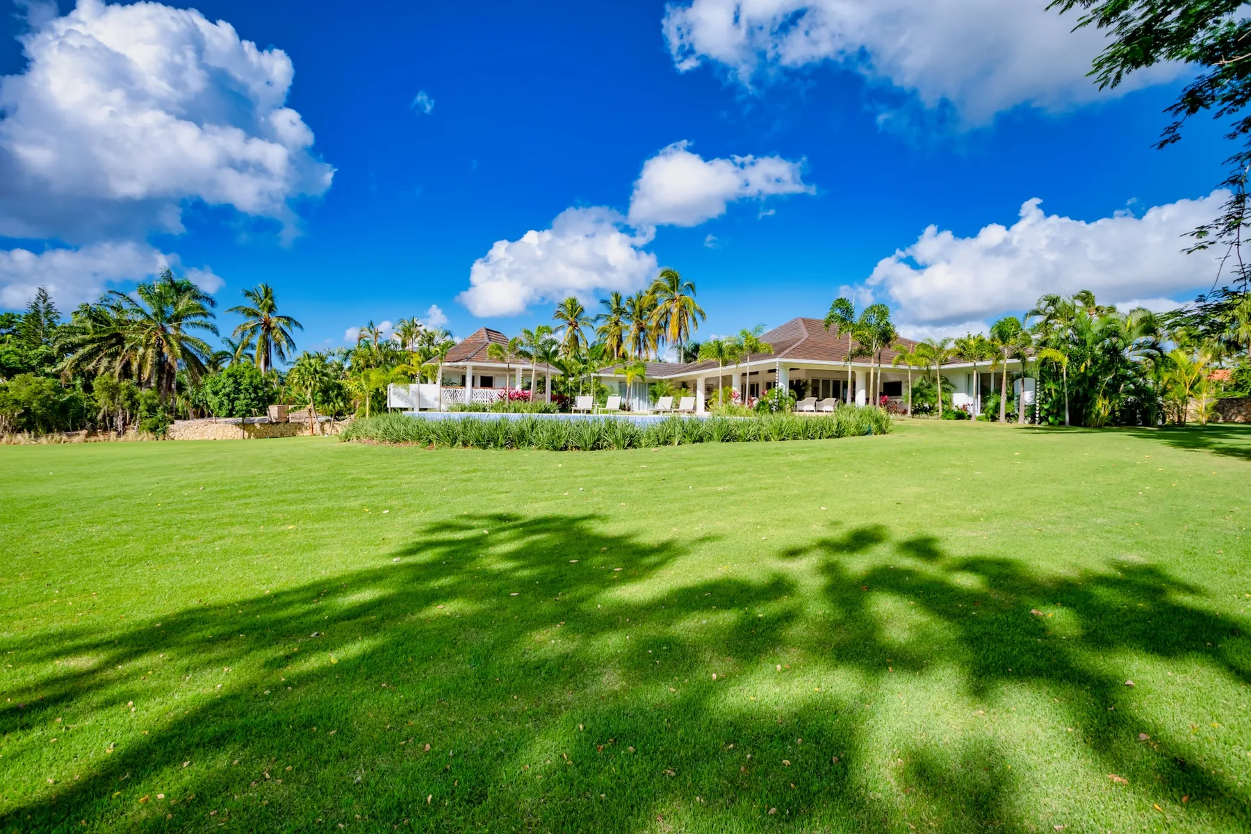 A low building sits beyond a broad green lawn beneath a bright blue sky.