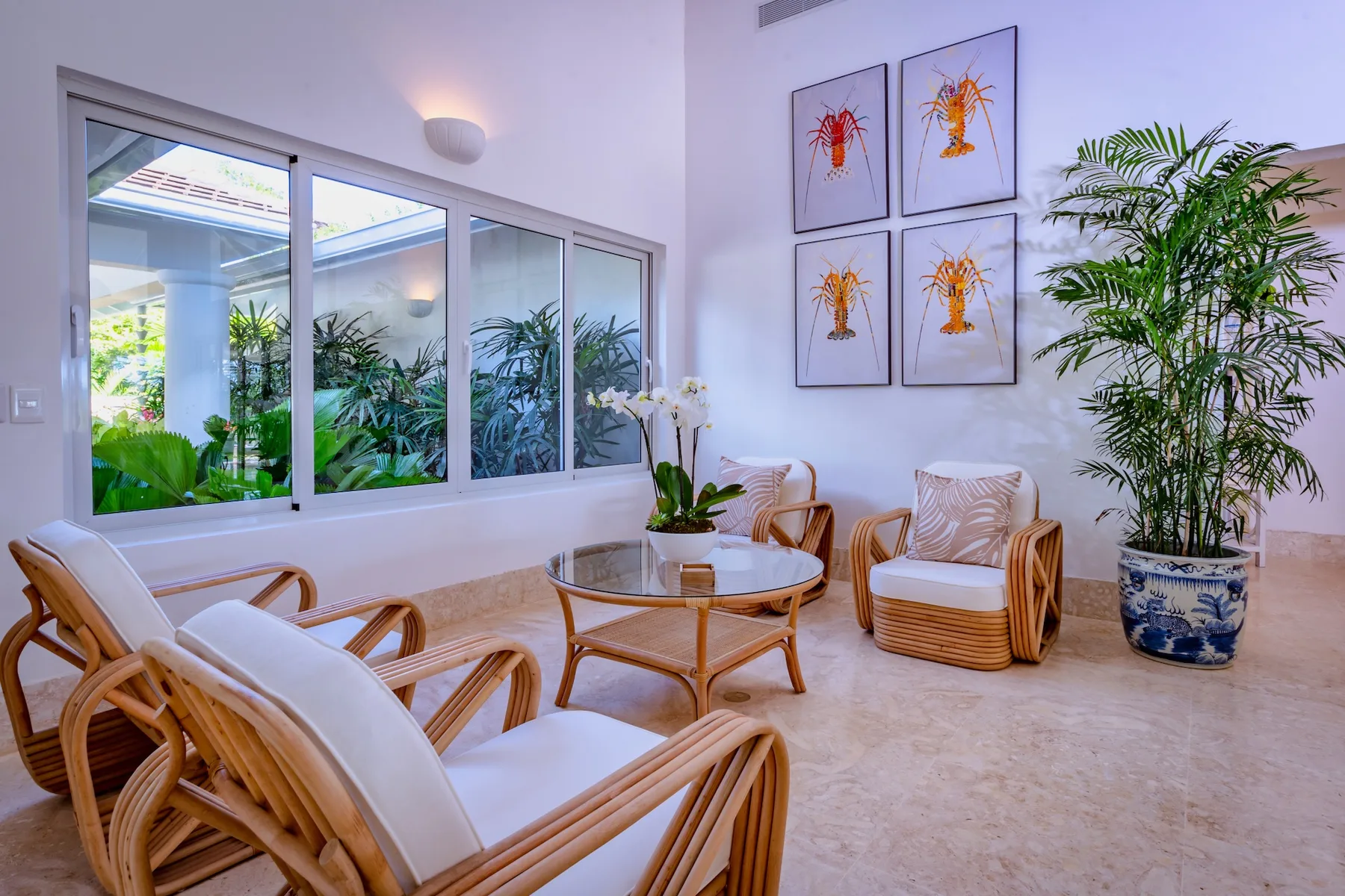 A bright sitting area with woven seating, a round table, and large windows.
