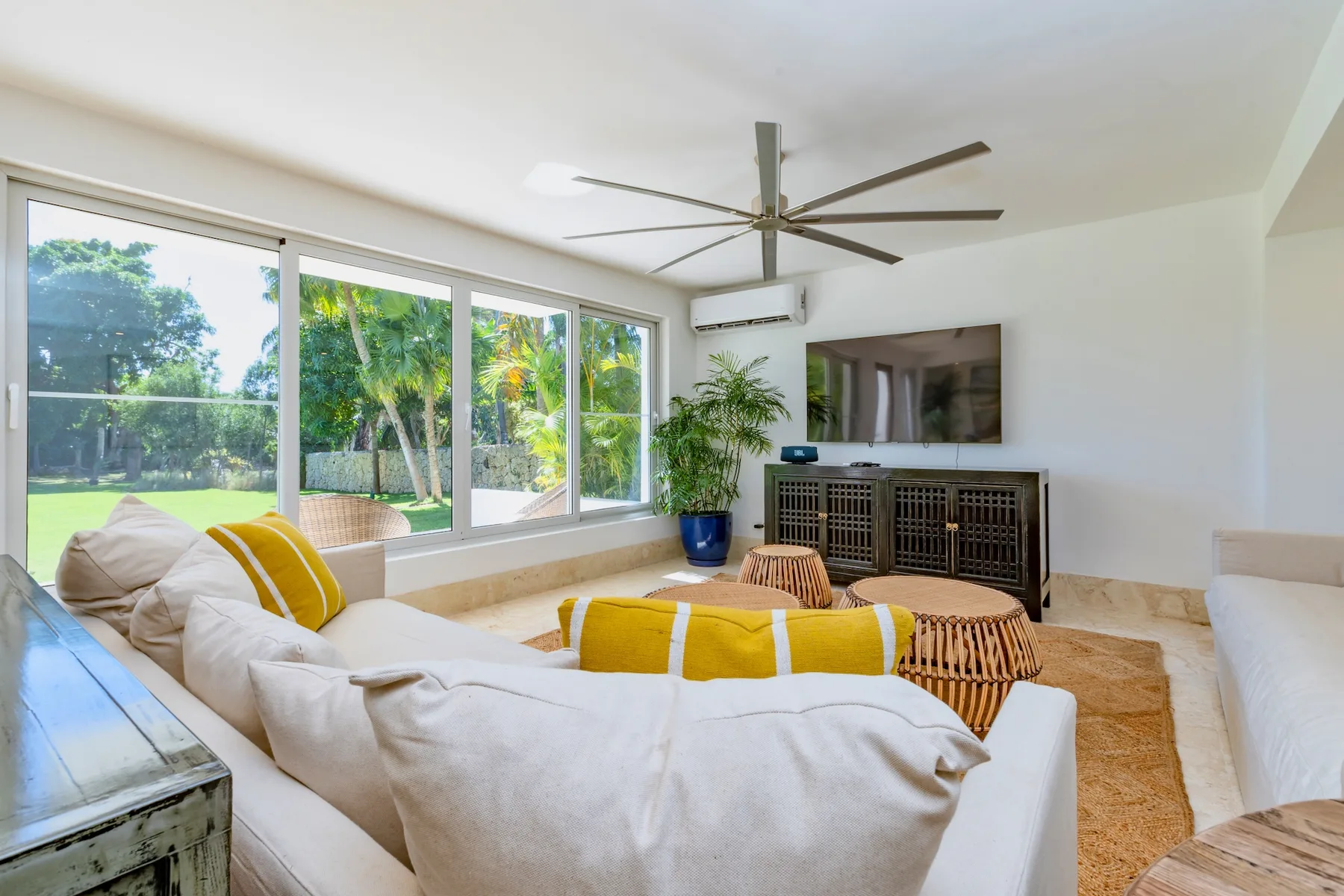 A bright living room with seating, large windows, and a television.
