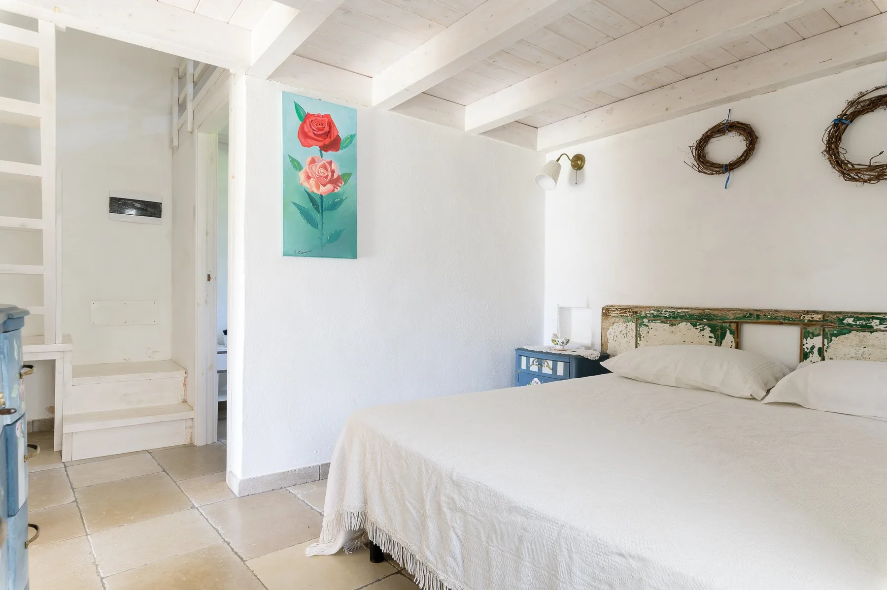 A bright bedroom with a large bed and floral artwork on the wall.