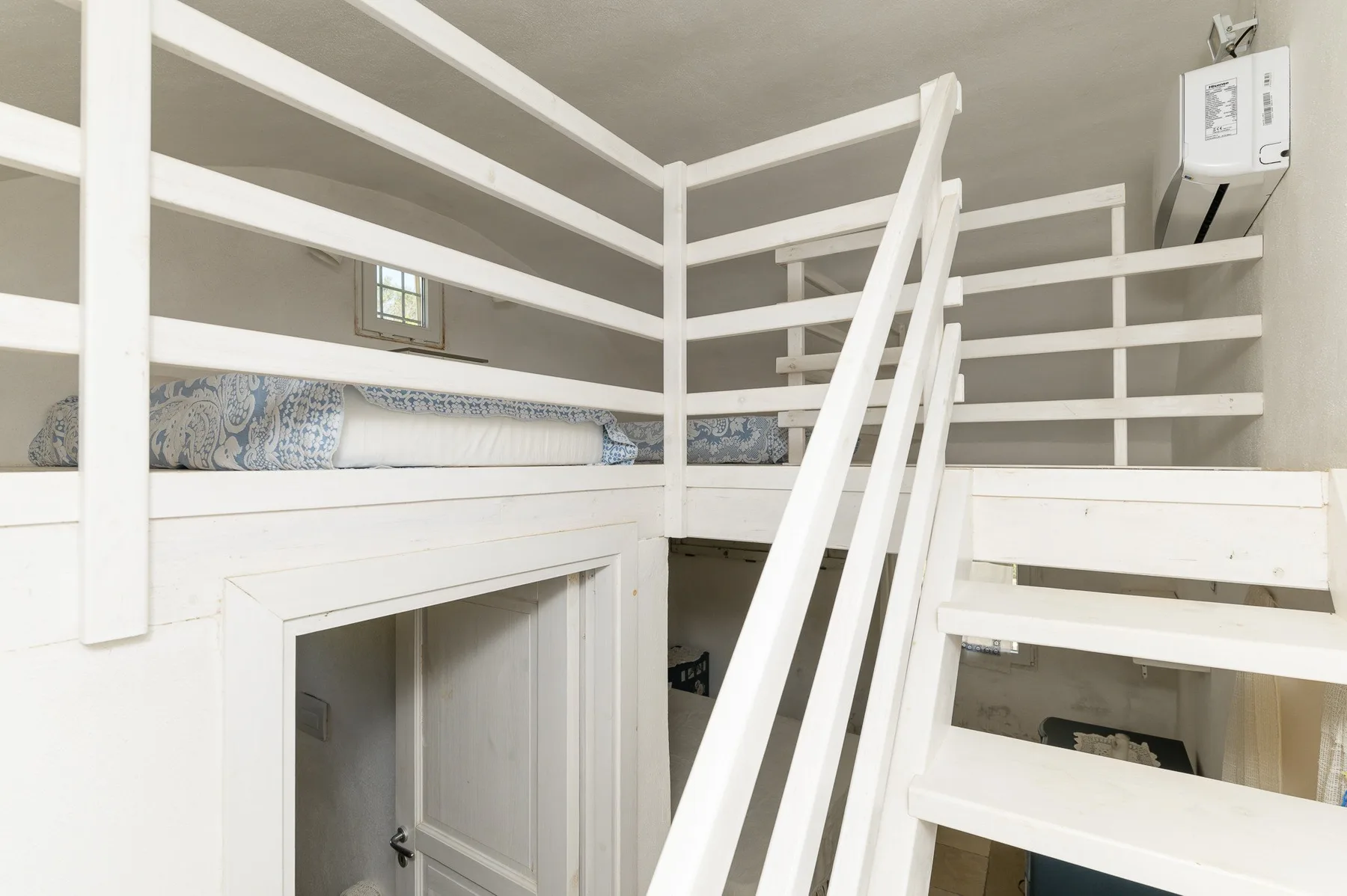 A white loft sleeping area with built-in bunks and a central ladder.