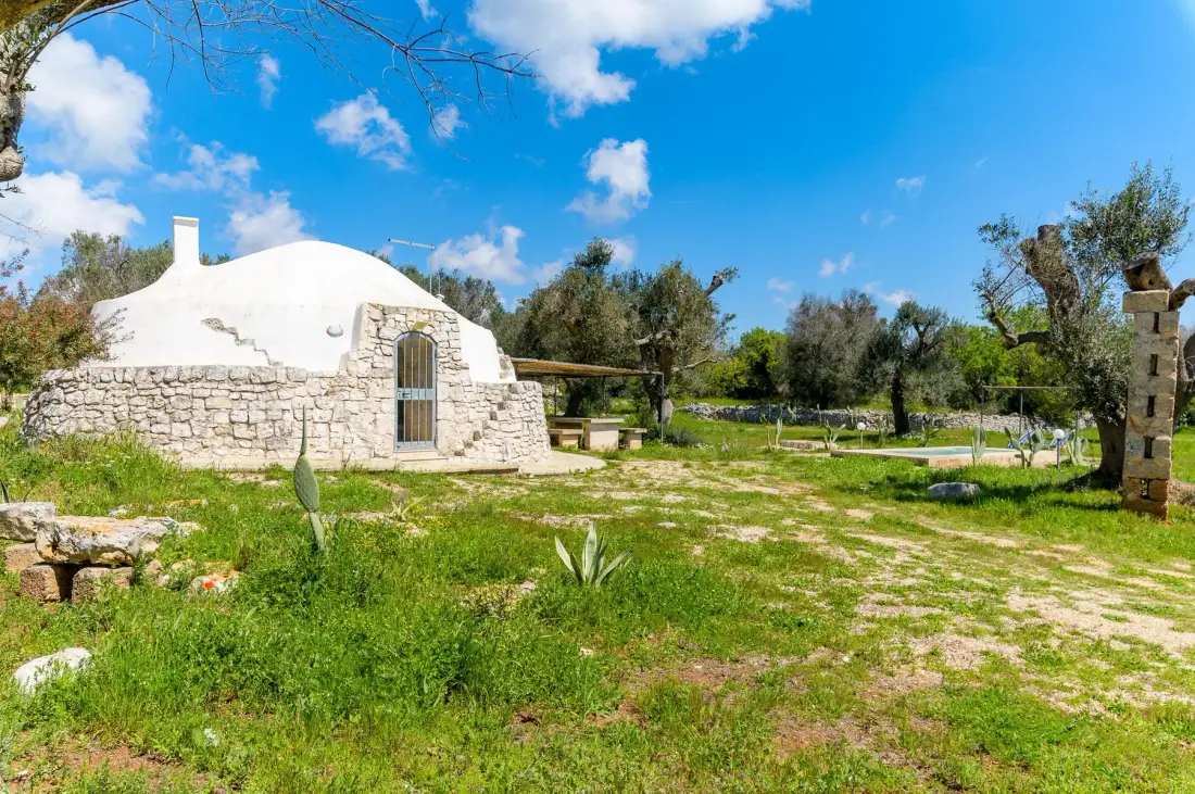 A white stone building stands in a grassy garden beneath a bright blue sky.
