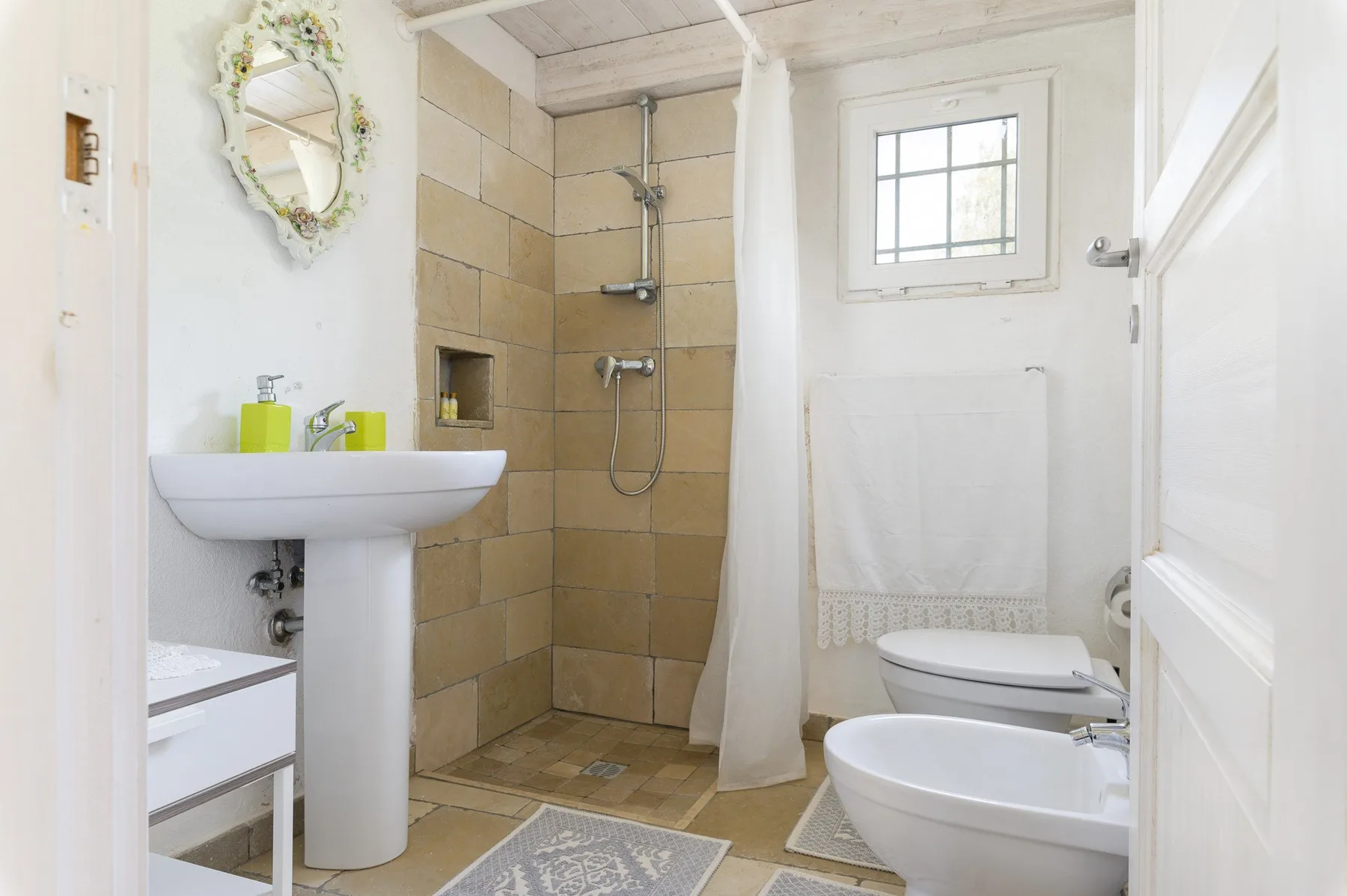 A bright bathroom with a tiled shower, pedestal sink, and bathtub.