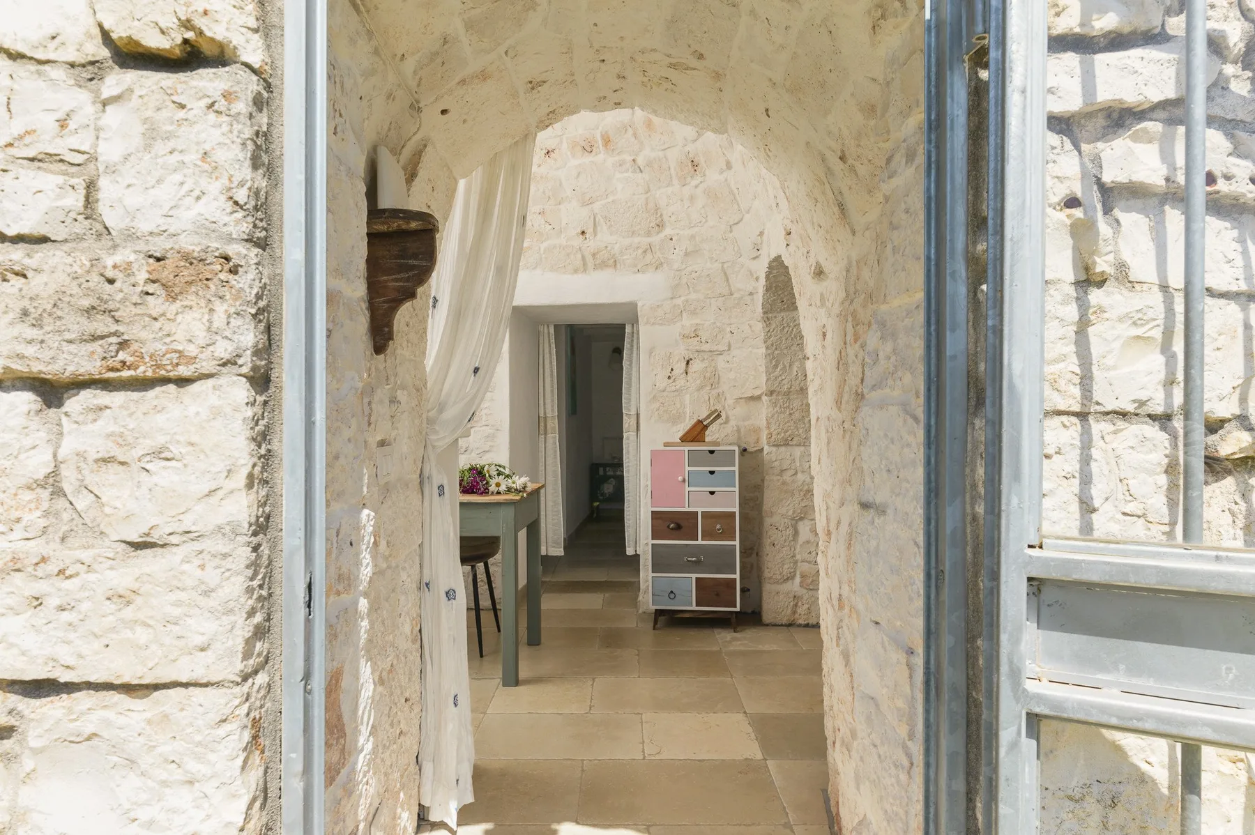 A stone hallway leads to an open doorway, with a small drawer unit nearby.