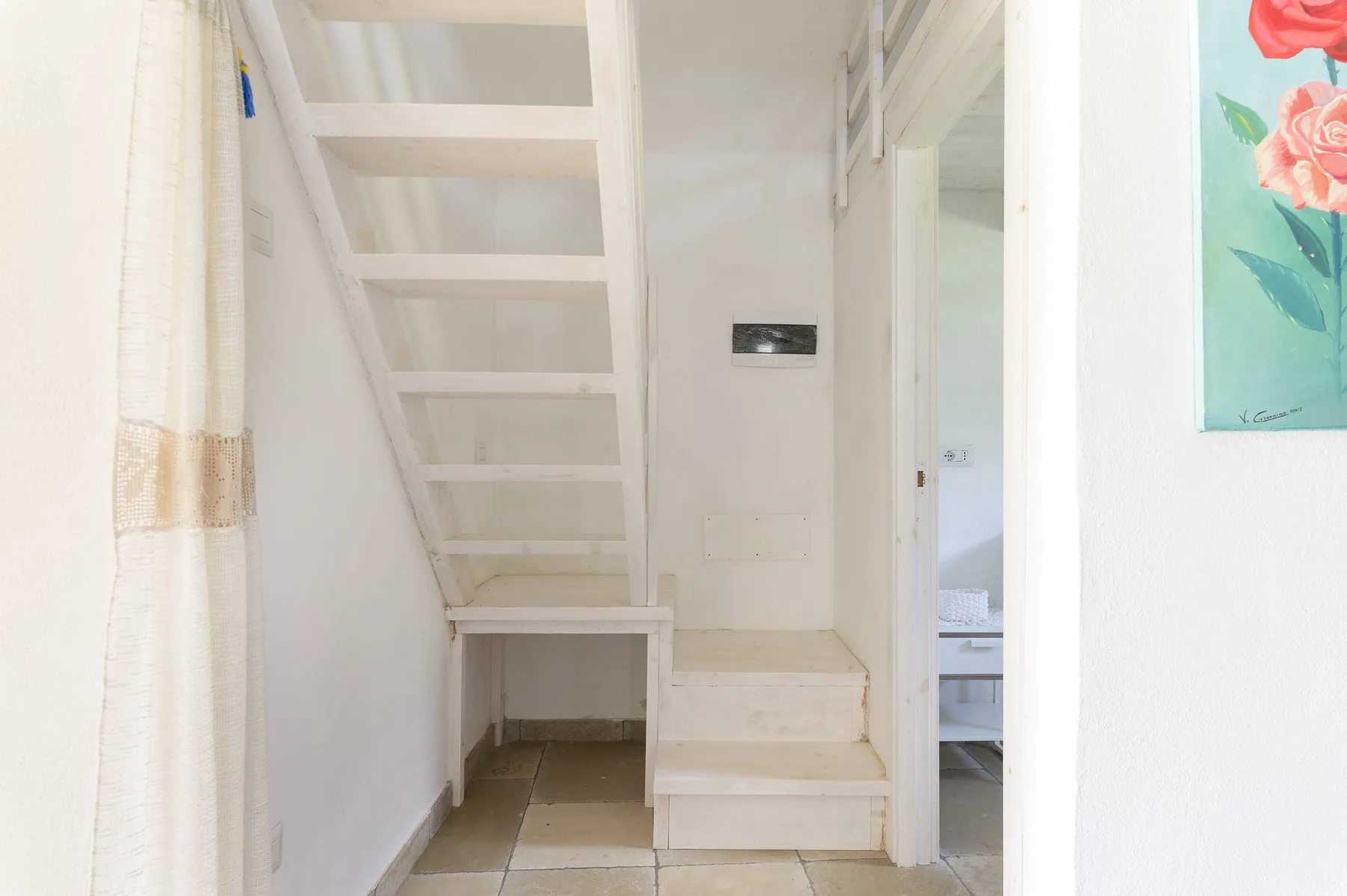 A narrow interior stairway rises beside a curtained window and an open doorway.