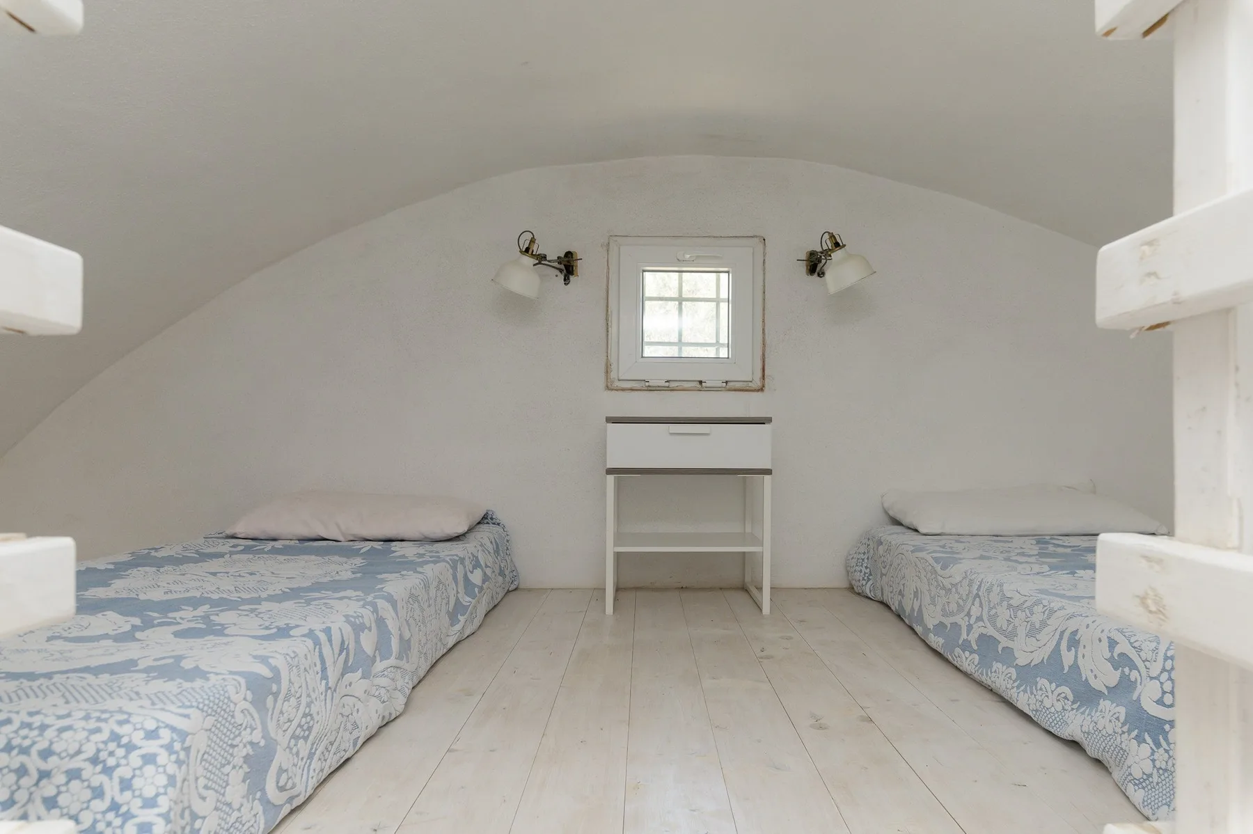 A bedroom with two beds and a small desk beneath a window.