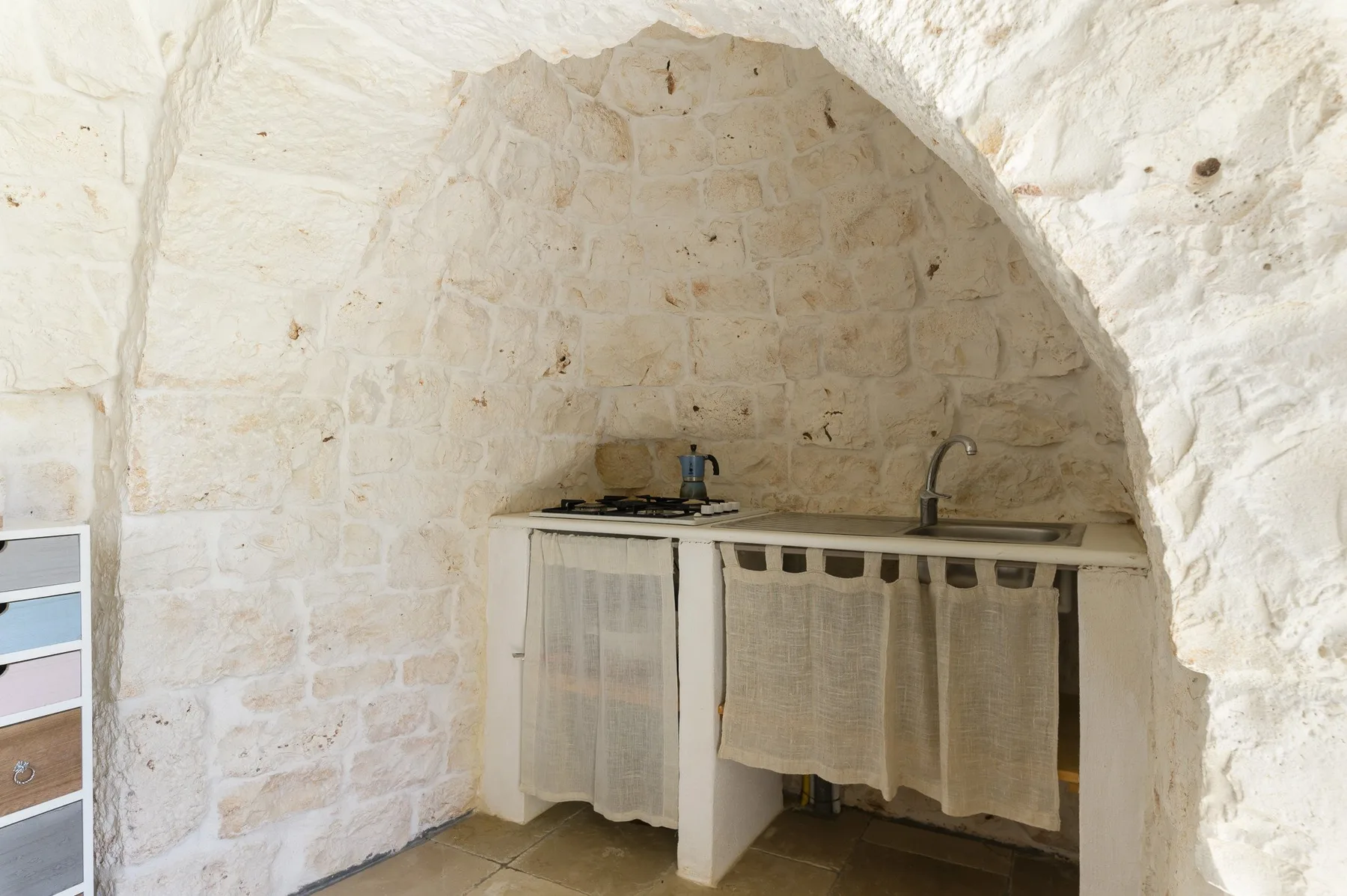 A small kitchen area sits beneath a pale stone arch, with a counter and sink.