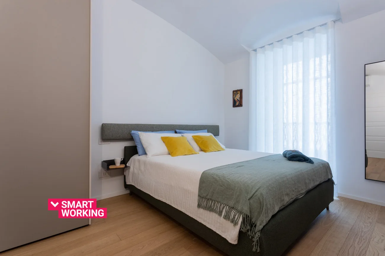 A bright bedroom with a neatly made bed and sheer curtains.