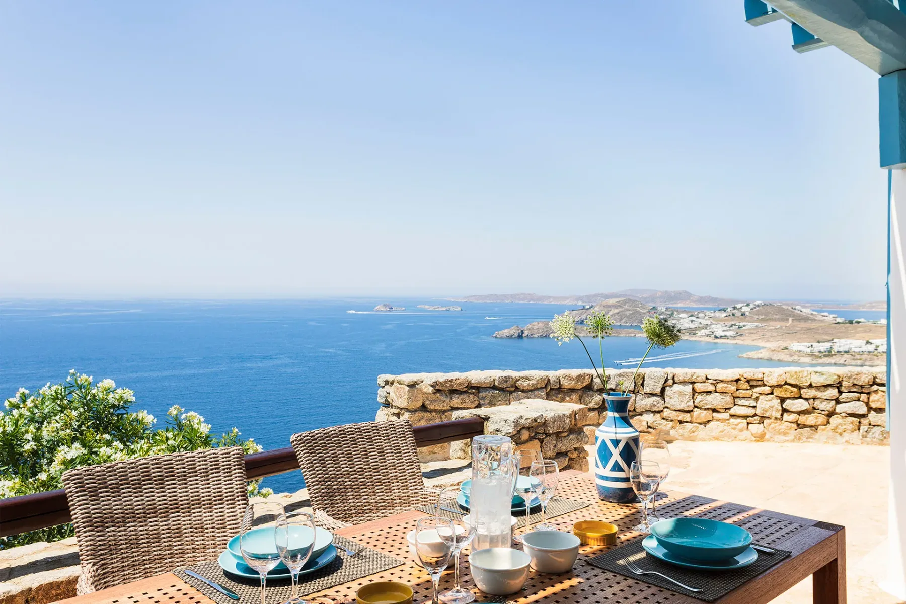 A seaside terrace dining table overlooks the blue water and distant coastline.