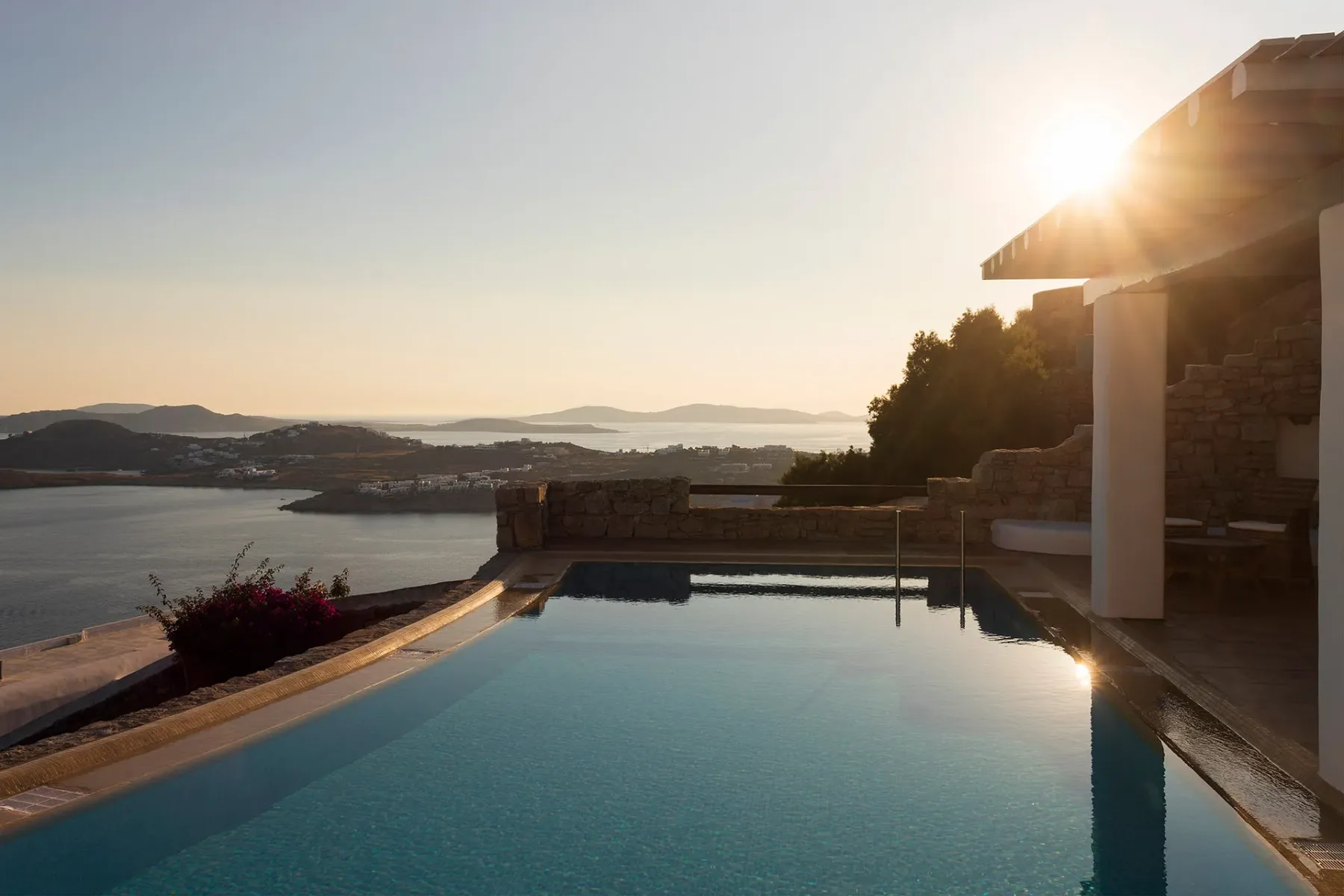 A swimming pool overlooks the water and distant hills in the evening sun.