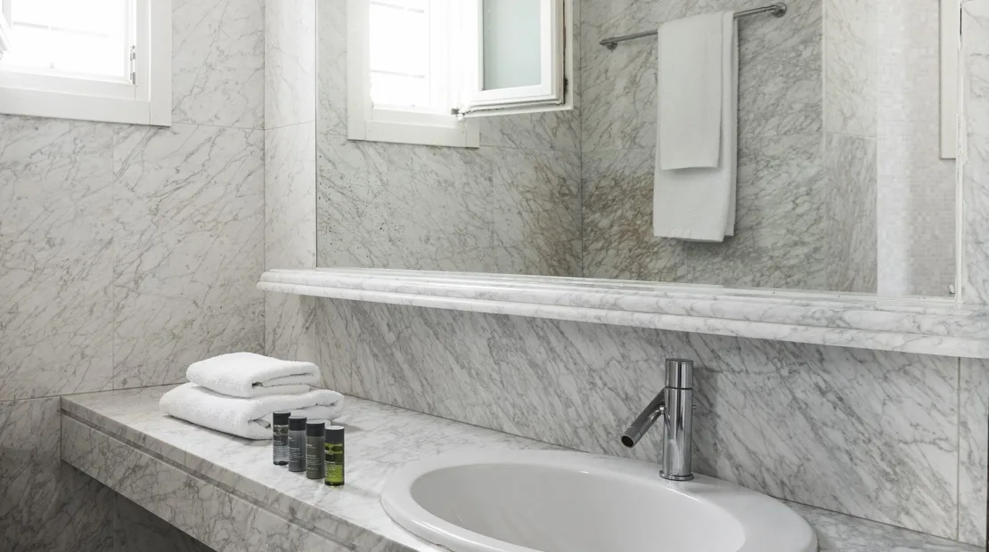 A marble bathroom vanity with an oval sink, towels, and a wall mirror.