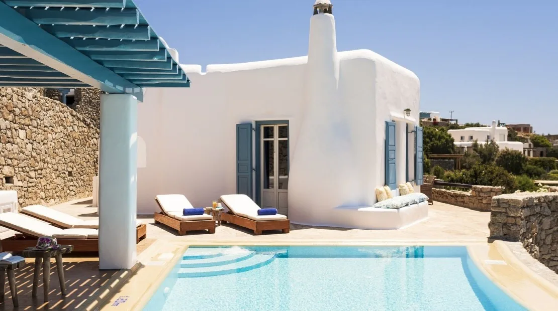 A white villa beside a swimming pool, with sun loungers on the patio.