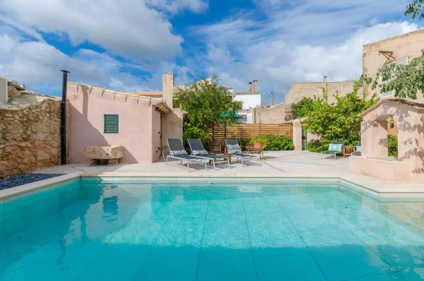 An outdoor swimming pool opens onto a paved courtyard with seating and greenery.