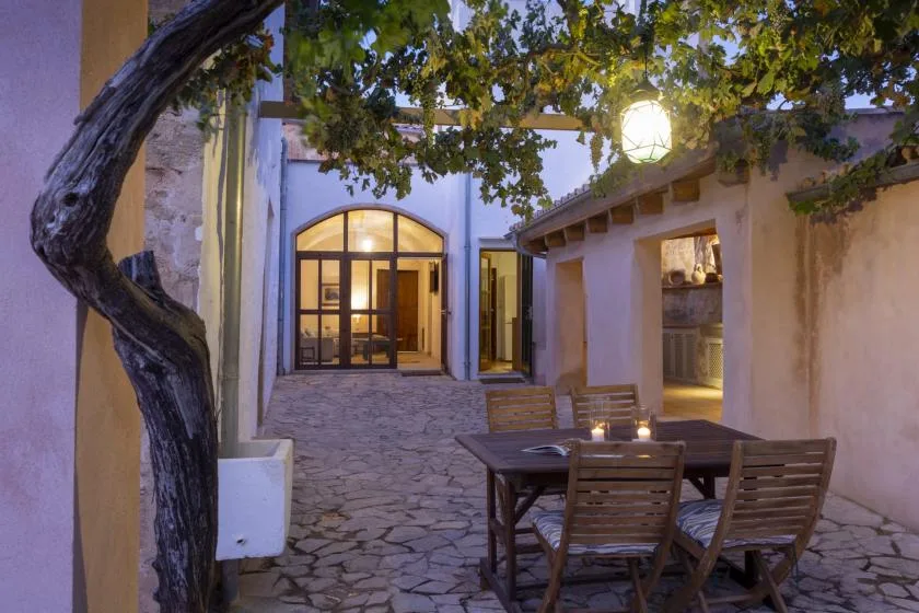 A paved courtyard with outdoor seating beneath a leafy tree at dusk.
