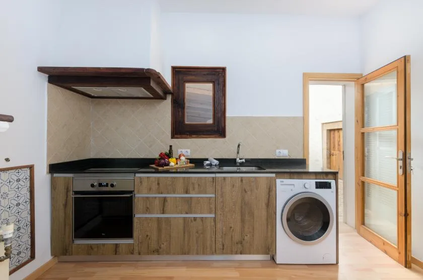 A compact kitchen with wood cabinetry, a dark countertop, and a washing machine.
