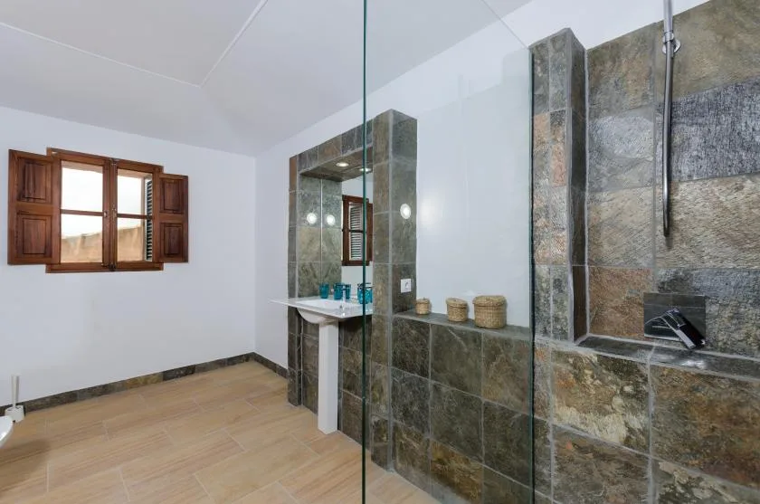 A bathroom with a glass shower, stone tile, and a window.