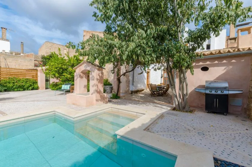 A sunlit courtyard with a swimming pool, shaded seating, and an outdoor grill.
