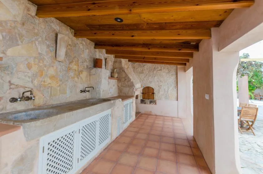 A stone outdoor kitchen with a long counter beneath exposed wooden ceiling beams.