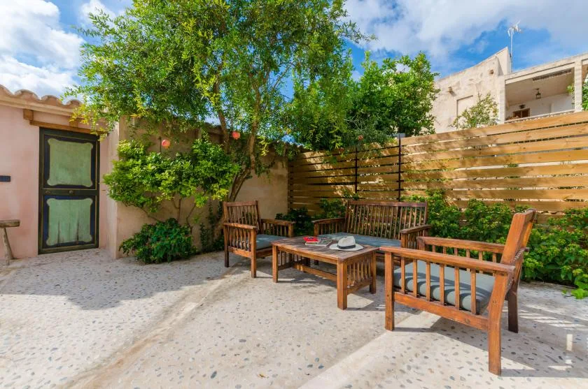 An outdoor patio with wooden seating and a table beneath leafy trees.