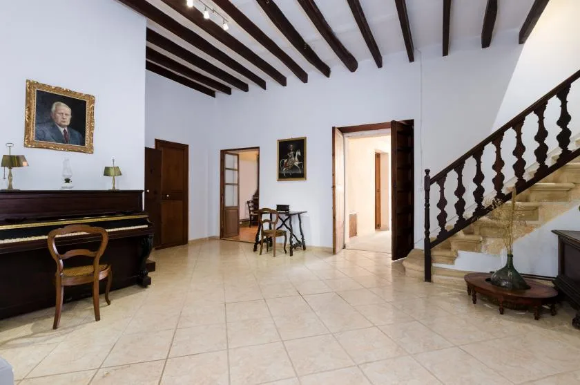 A spacious interior hall with a piano, dining table, and staircase.