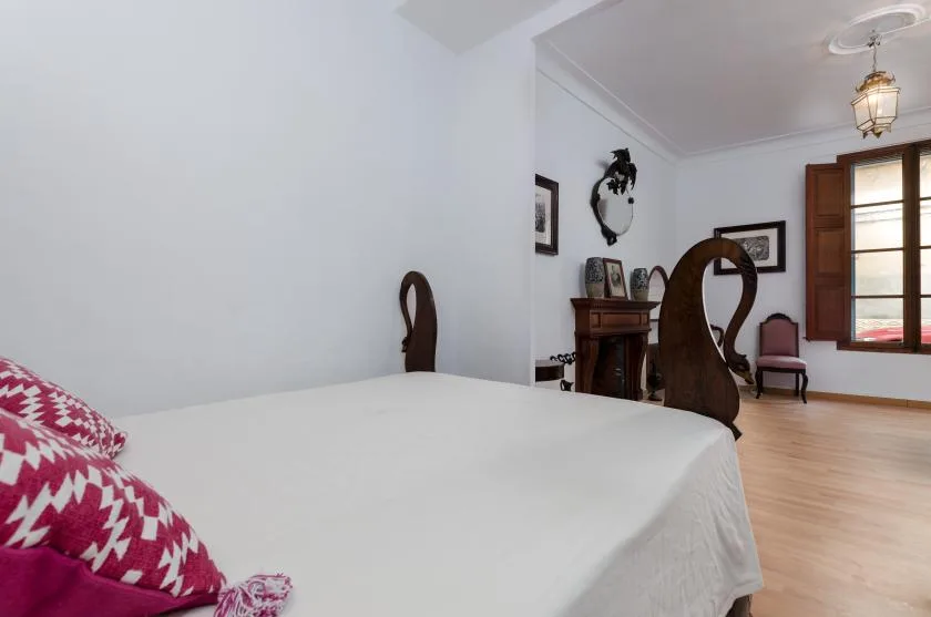 A bedroom with a bed, patterned pillows, and a wooden desk near a window.