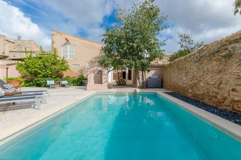 An outdoor swimming pool sits beside a stone wall and shaded seating area.