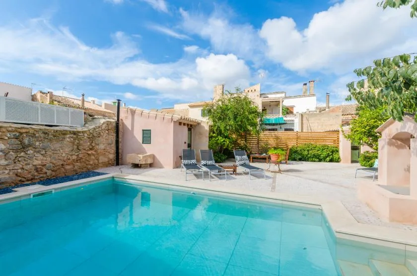 An outdoor swimming pool beside a paved patio with lounge seating.