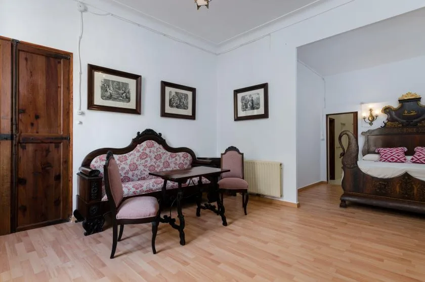 A bedroom sitting area with patterned seating, framed pictures, and a bed.