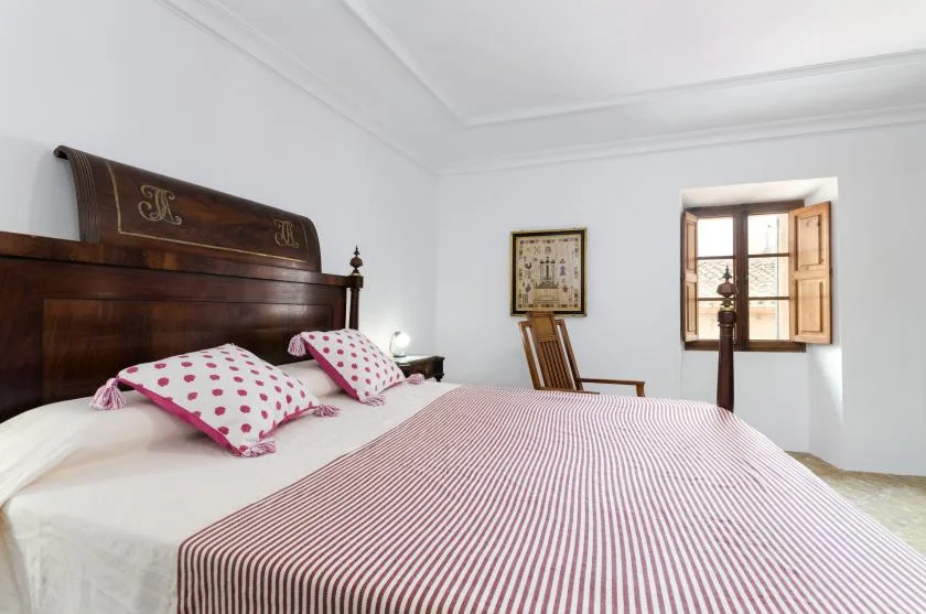 A bedroom with a wooden bed, striped bedding, and an open window.