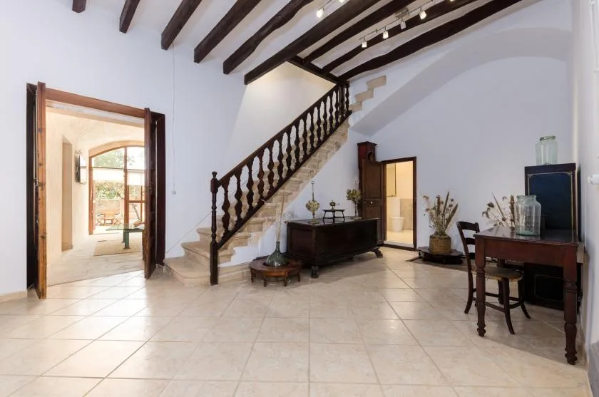 A bright interior hall with a staircase and dark exposed ceiling beams.