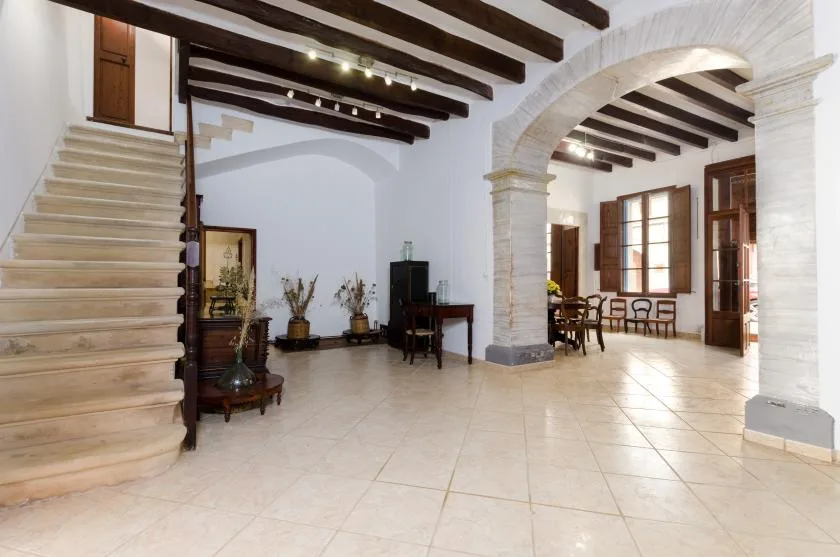 A spacious interior hall with a staircase, exposed ceiling beams, and an arched opening.