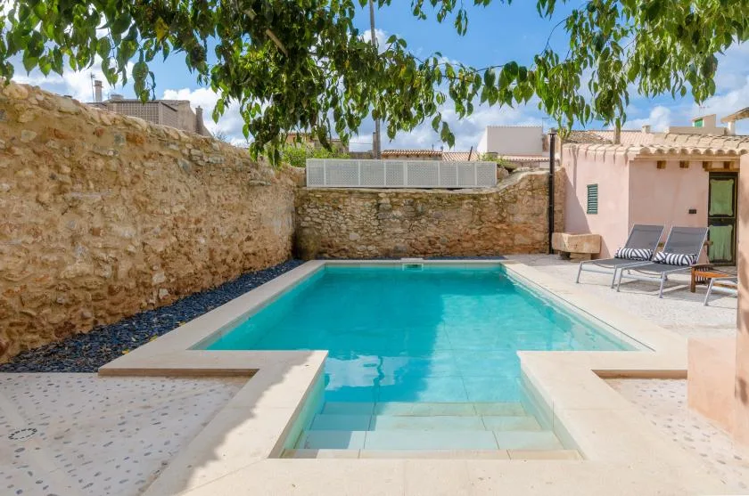 A courtyard swimming pool sits beside stone walls and outdoor seating.