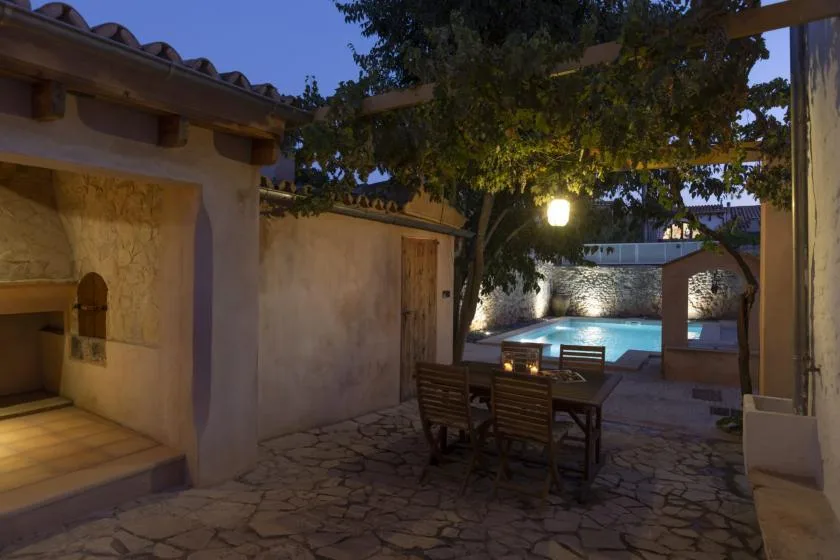 A stone-paved courtyard with outdoor seating and a swimming pool at dusk.