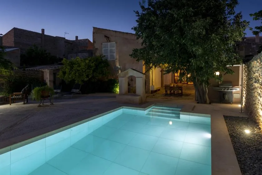 An illuminated swimming pool beside a landscaped patio at dusk.