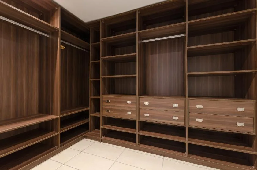 A walk-in closet with dark wood shelving, hanging space, and drawers.