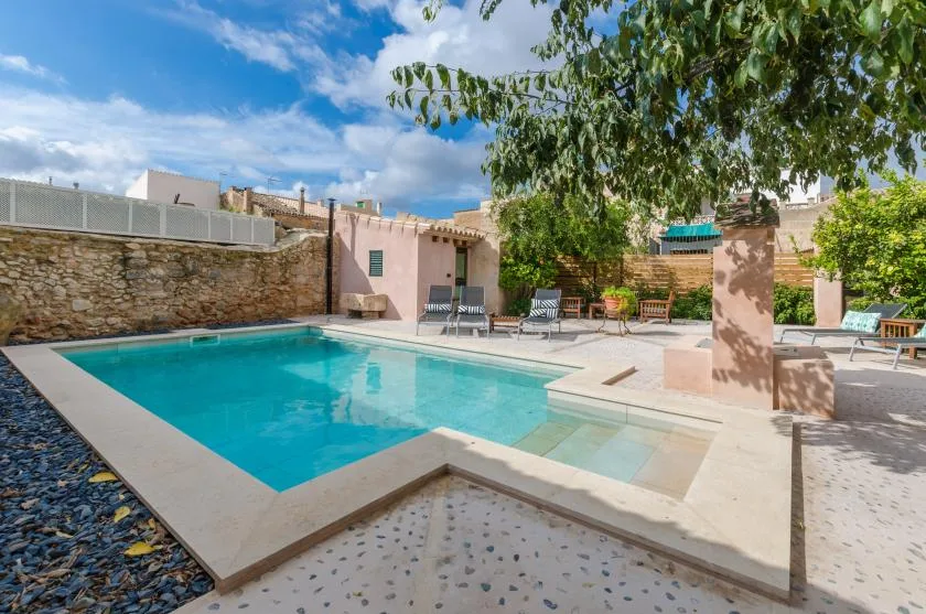 An outdoor swimming pool beside a stone wall and shaded seating area.