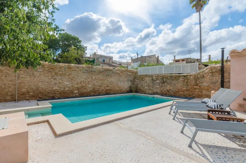An outdoor swimming pool beside a stone wall, with sun loungers on the patio.