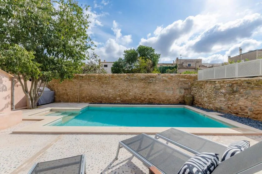 An outdoor swimming pool sits beside a paved patio and lounge seating.