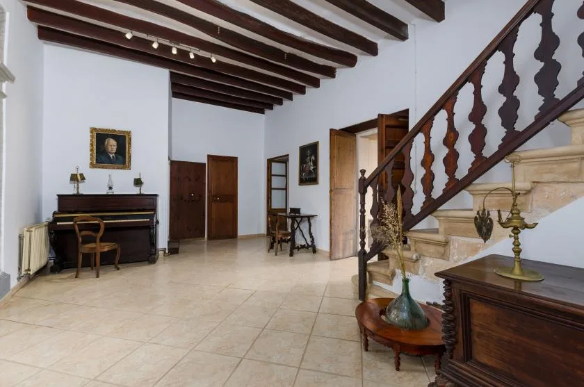 A spacious interior hall with a staircase, tiled floor, and dark wooden ceiling beams.
