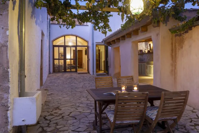 A stone-paved courtyard with a wooden dining table beneath leafy vines.