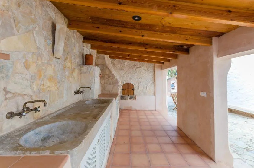 A rustic kitchen with a long stone counter beneath exposed wooden ceiling beams.