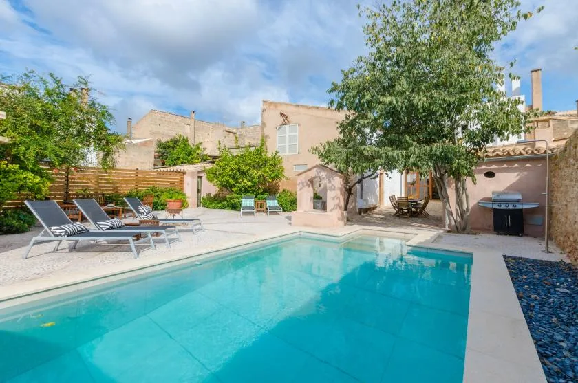 An outdoor swimming pool beside a patio with lounge seating and trees.